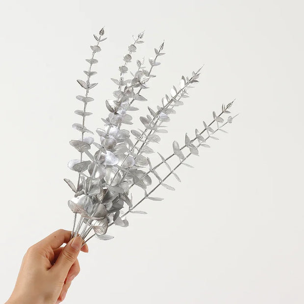 Hand holding a branch of silver eucalyptus leaves against a light gray background