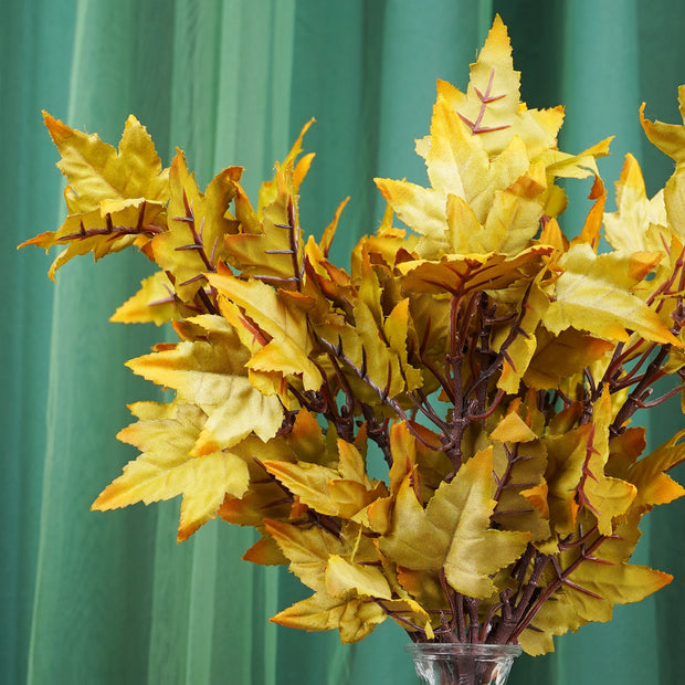 Artificial plant with yellow and brown leaves in a clear vase against a green curtain background