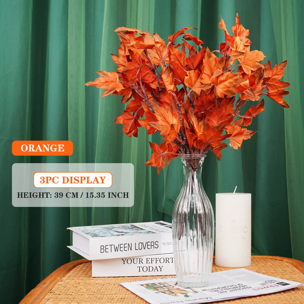 Orange artificial leaves in a clear vase on a table with a green curtain background