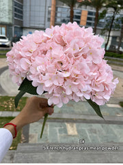 Bouquet of pink hydrangeas held by a person outdoors.