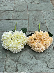 Two flower bouquets, one white and one beige, on a stone pavement.