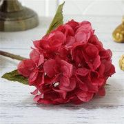 Red artificial flower arrangement on a white wooden surface