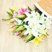Bouquet of white, pink, and yellow lilies on a wooden surface with a book in the background.