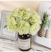 Green flowers in a decorative vase on a table with a pineapple and framed picture in the background.