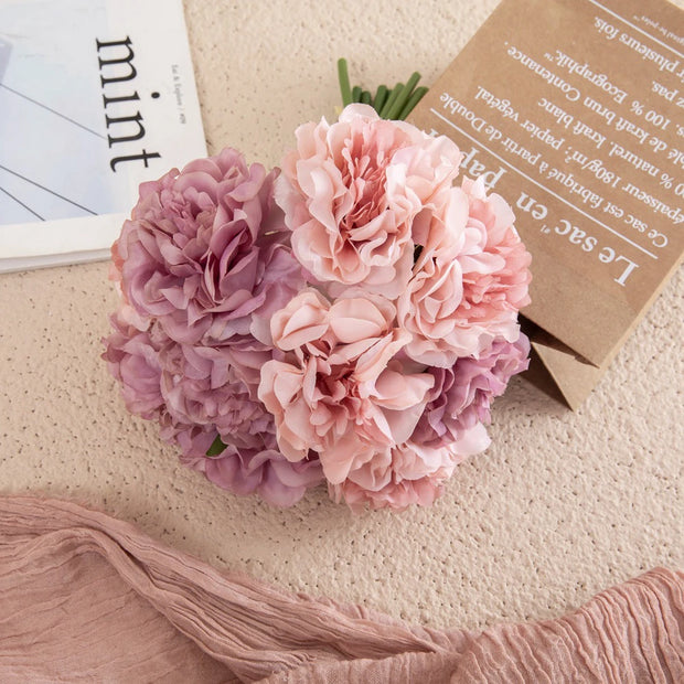 Pink and purple flowers on a light surface with a magazine and paper in the background
