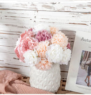 Bouquet of pink, white, and peach flowers in a textured white vase on a wooden surface with a magazine.