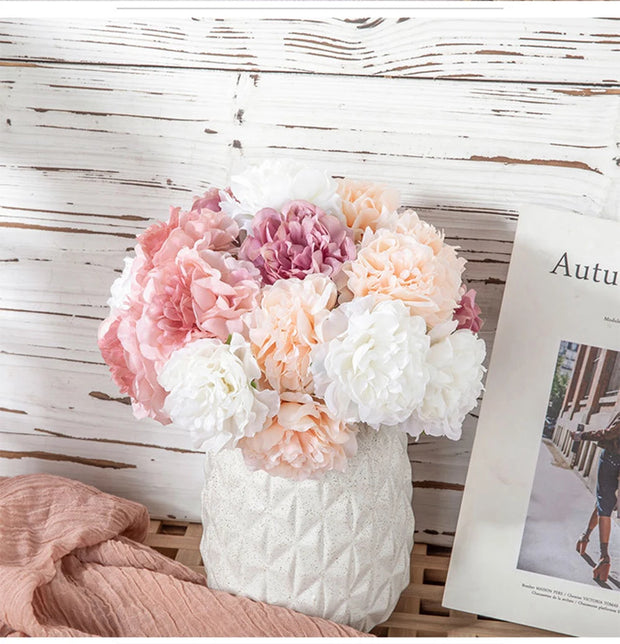 Bouquet of pink, white, and peach flowers in a textured white vase on a wooden surface with a magazine.