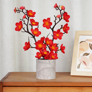 Red floral arrangement in a gray vase on a wooden surface with a light gray curtain background.