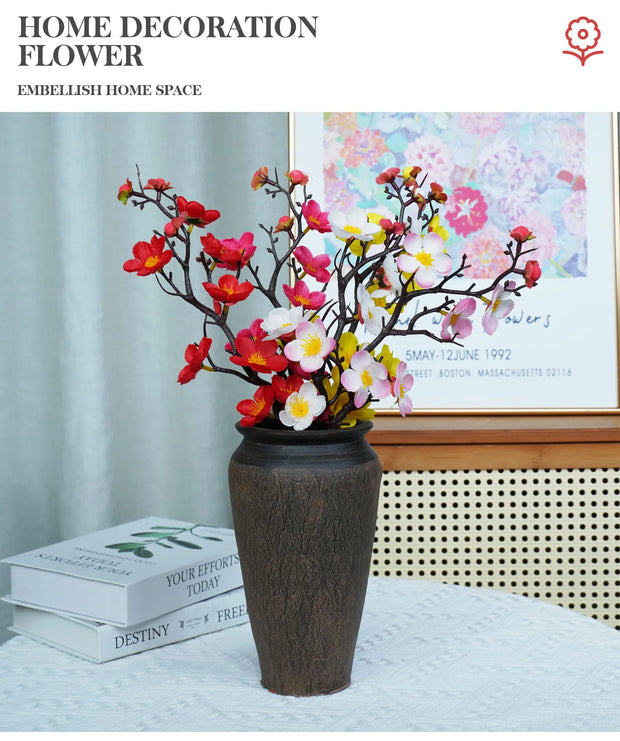 Decorative flower arrangement in a vase on a table with books and a framed picture in the background.