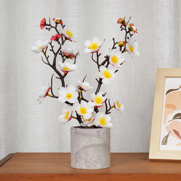 Decorative artificial flower branch in a gray vase on a wooden surface with a light gray wall background.