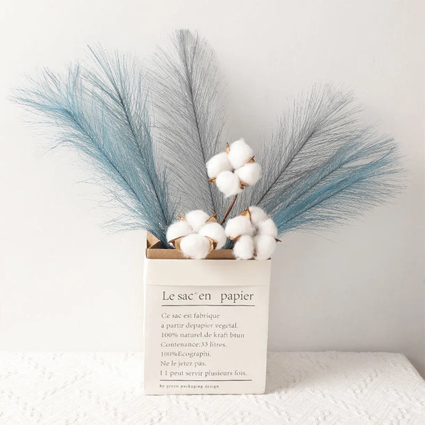 Decorative arrangement with cotton and blue feathers in a paper bag on a white surface.