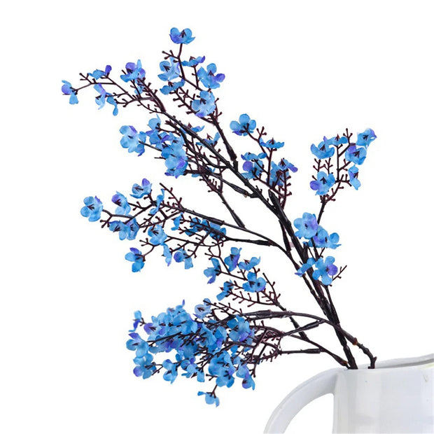 Blue artificial flowers on black stems in a white vase against a white background