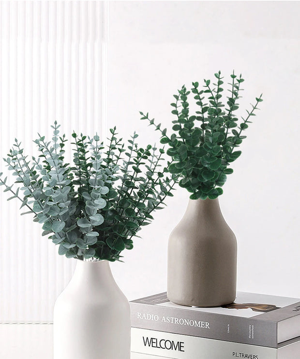 Two vases with green foliage on a white surface
