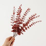 Hand holding a bouquet of red artificial leaves against a white background