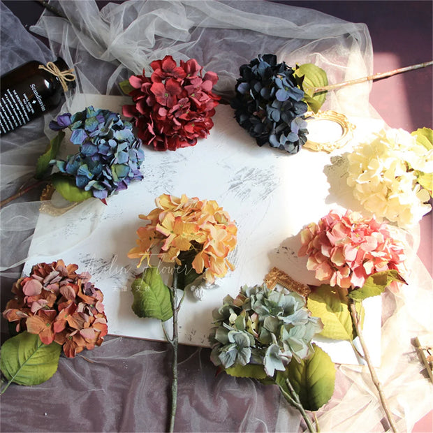 Colorful artificial flowers on a white surface with a bottle in the background