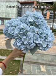 Bouquet of blue hydrangeas held by a person outdoors.
