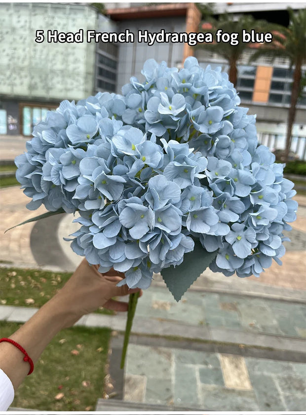 Bouquet of blue hydrangeas held by a person outdoors.