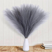 White vase with dried gray grasses against a light wooden panel background