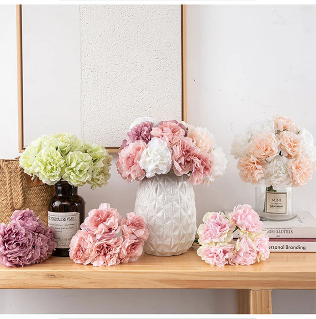 Decorative flowers in vases on a wooden surface with a neutral background
