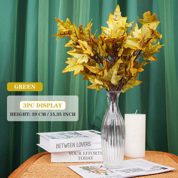Decorative yellow leaf arrangement in a clear vase on a table with green curtain background