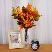 Vase with autumn leaves, alarm clock, and photo frame on a wooden surface.
