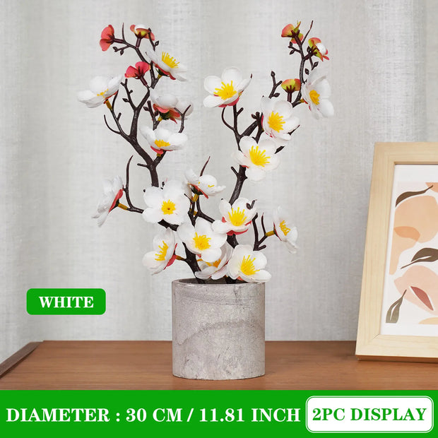 Decorative floral arrangement in a gray pot on a wooden surface with a neutral background