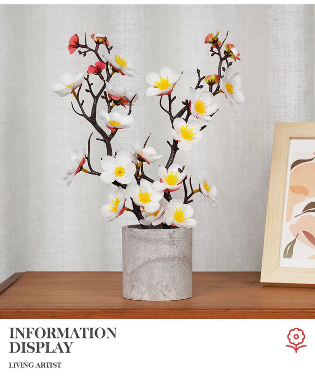 Decorative plant in a pot on a wooden surface with a framed picture in the background.