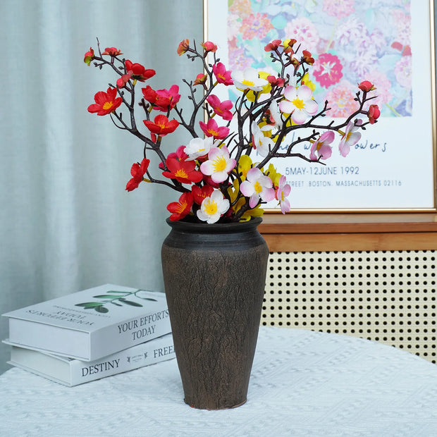 Decorative vase with colorful flowers on a surface, with books and a framed picture in the background.