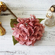 Pink artificial flower arrangement on a white wooden surface with decorative elements.
