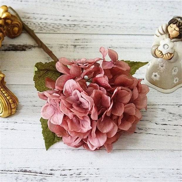 Pink artificial flower arrangement on a white wooden surface with decorative elements.