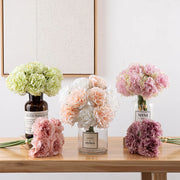 Three vases with flowers on a wooden surface against a light wall.