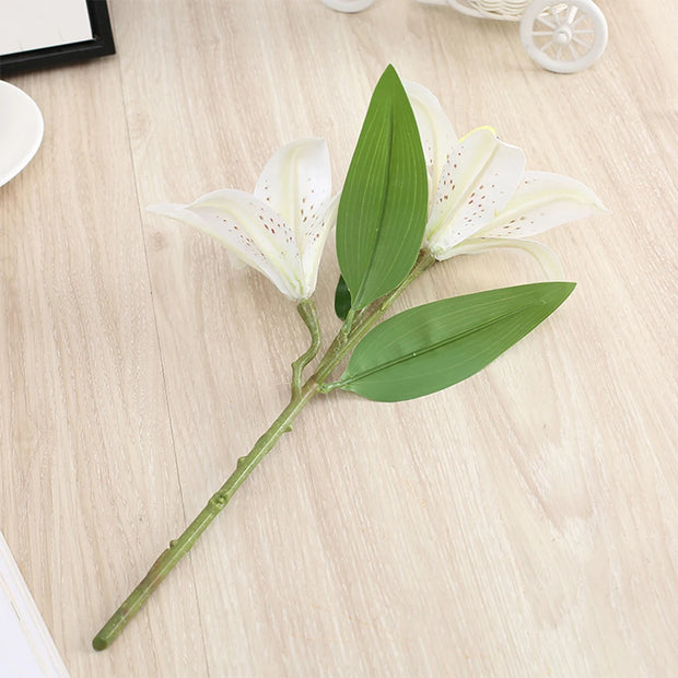 Artificial white lily flower with green leaves on a light wooden surface