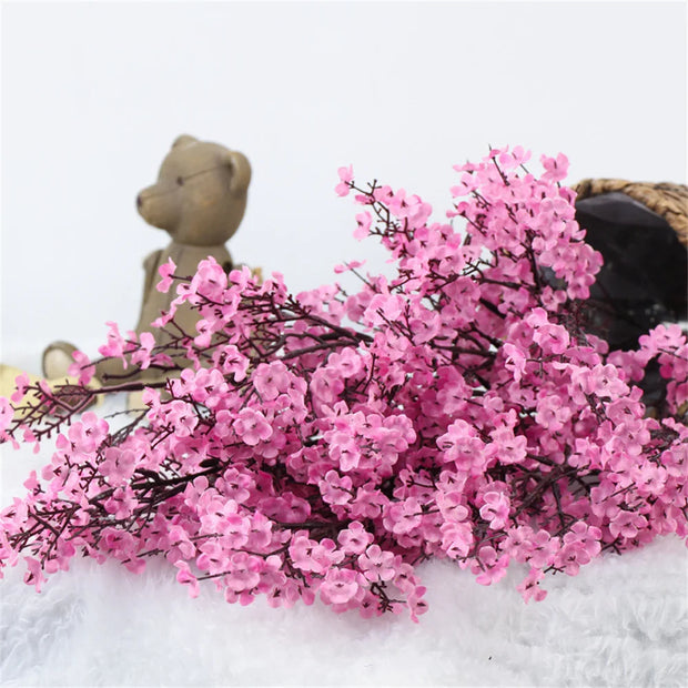 Pink artificial flowers with a teddy bear and woven basket on a white background