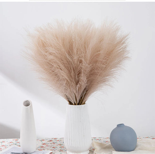 Decorative arrangement of pampas grass in a white vase with two other vases on a light surface.
