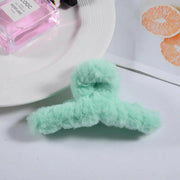Green fuzzy hair tie on a white surface with a pink bottle and orange slices in the background.