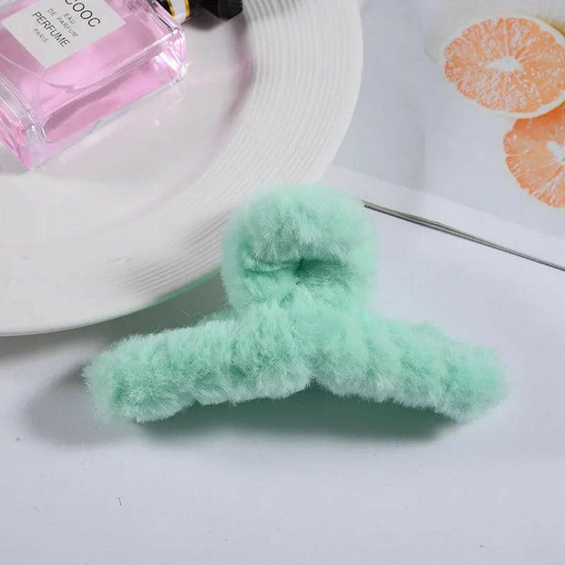 Green fuzzy hair tie on a white surface with a pink bottle and orange slices in the background.