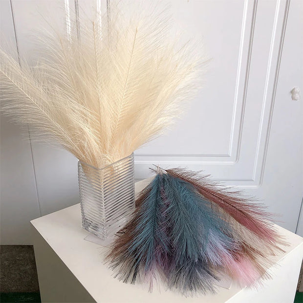 Decorative pampas grass in a clear vase on a white surface with a white wall background.