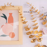 Decorative gold eucalyptus branch next to a framed illustration of vases on a magazine page.