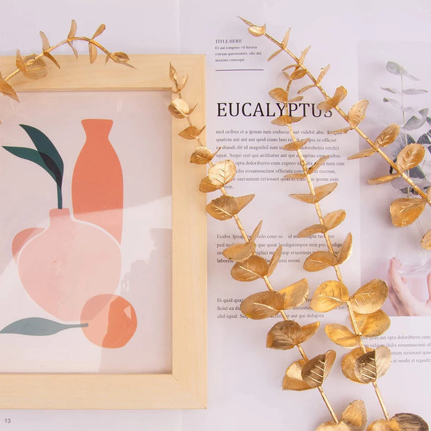 Decorative gold eucalyptus branch next to a framed illustration of vases on a magazine page.