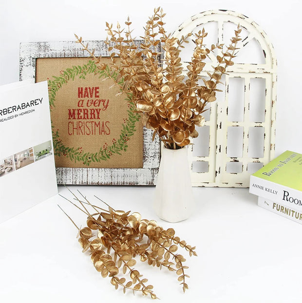 Decorative setup with a Christmas card, vase with gold foliage, and books on a white surface.