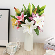 Bouquet of colorful lilies in a white vase on a wooden surface with books and a small decorative cart in the background.