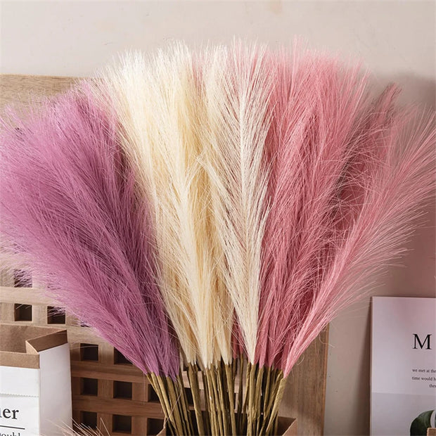 Bouquet of pink and beige dried grasses in a wooden basket against a neutral background.