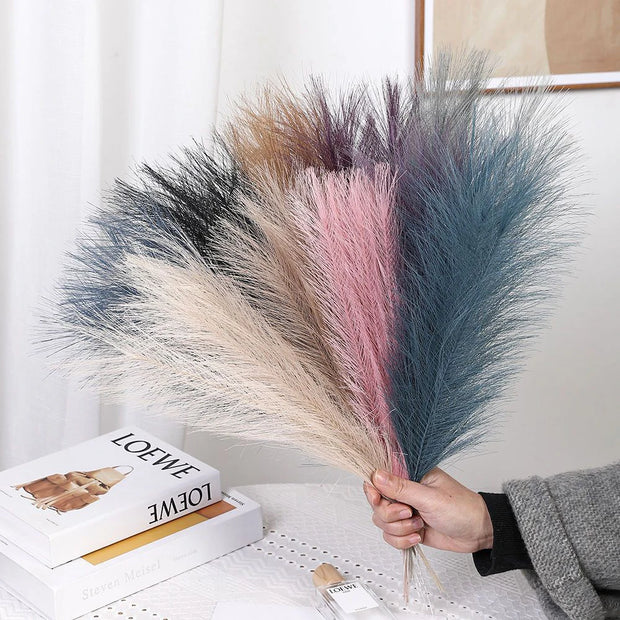 Bouquet of dried pampas grass held by a person with a book and perfume bottle in the background.