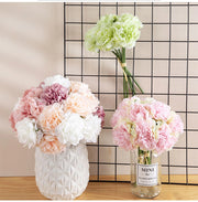 Three vases with floral arrangements on a wooden surface against a grid-patterned wall.