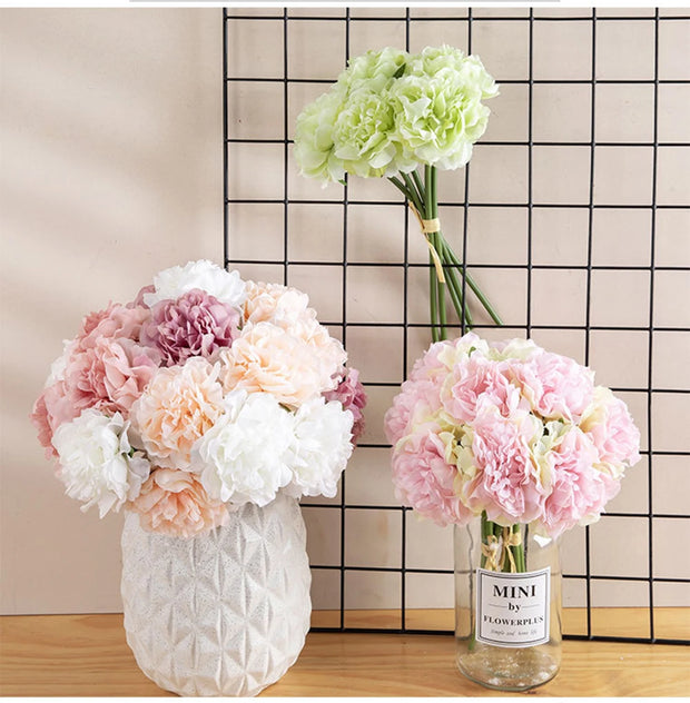 Three vases with floral arrangements on a wooden surface against a grid-patterned wall.