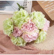 Bouquet of pink and green flowers on a textured surface with a magazine in the background.