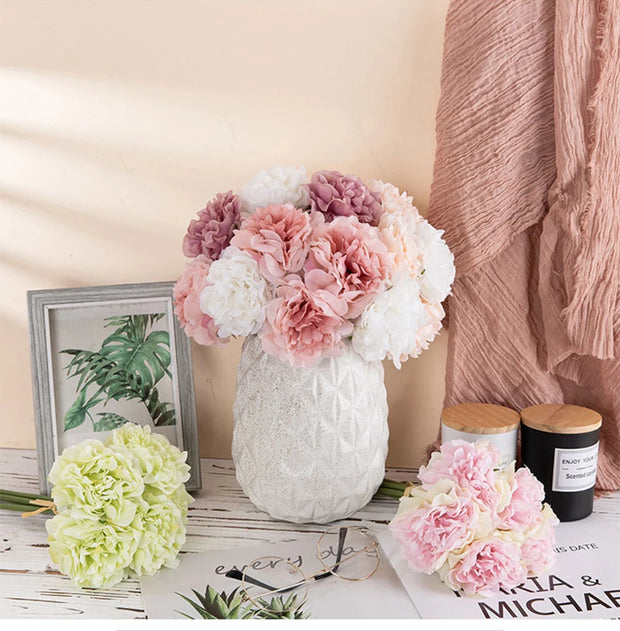Decorative setting with flowers in a white vase, candles, and a photo frame on a wooden surface.