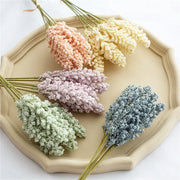 Five small bouquets of dried flowers in pastel colors on a beige hexagonal plate.