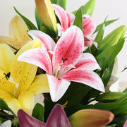Bouquet of pink, yellow, and white lilies with green leaves.