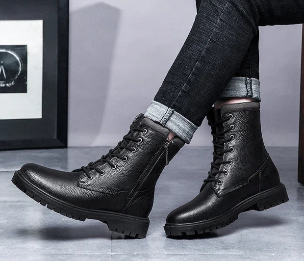 Black leather boots worn with rolled-up jeans on a neutral background
